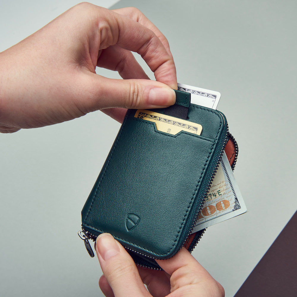 Person opening a teal leather wallet with money sticking out, on a light gray background
